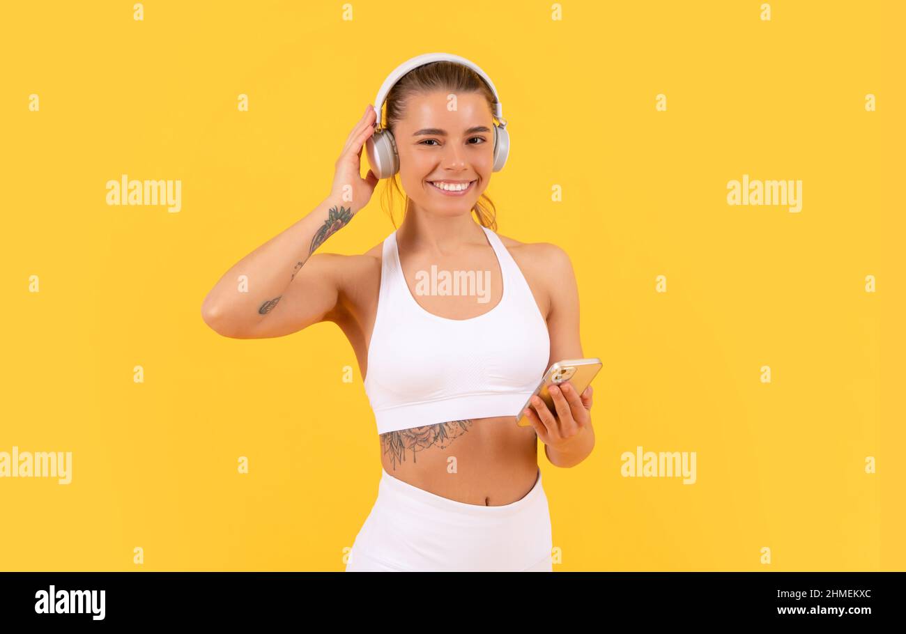 donna sportiva felice con cuffie e smartphone su sfondo giallo Foto Stock