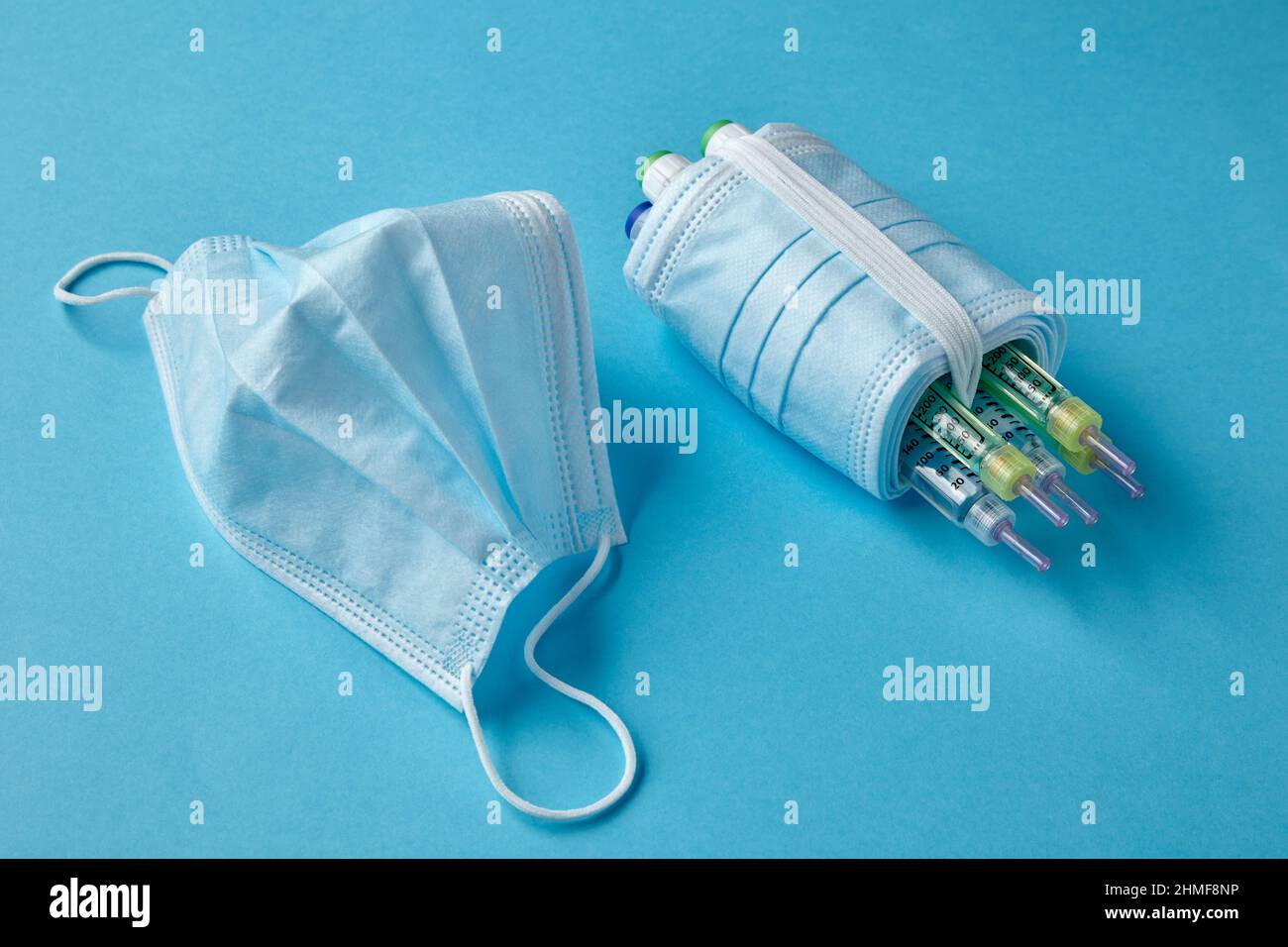 Penne per siringhe per insulina avvolte con maschere mediche su sfondo blu Foto Stock