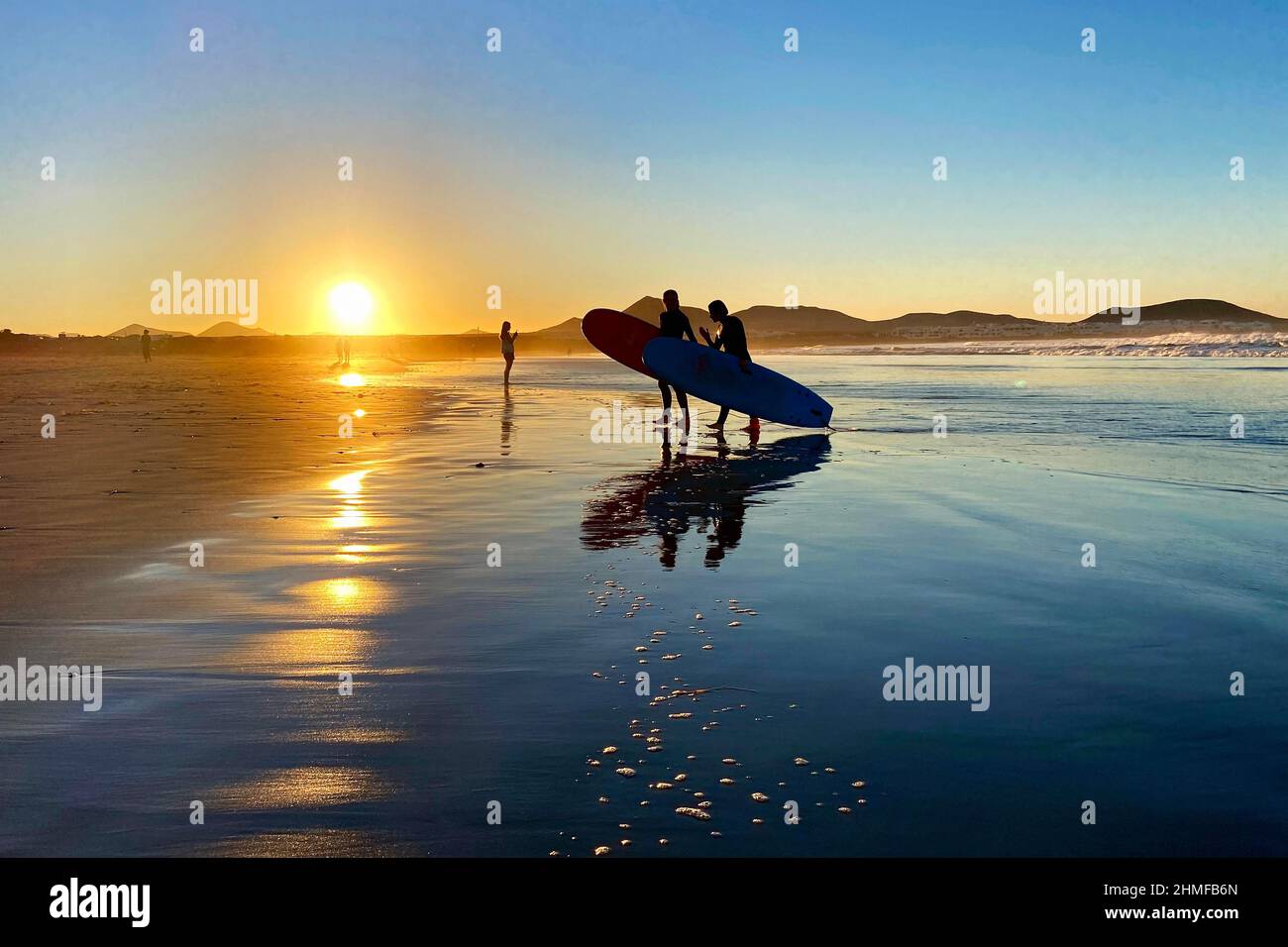 Surfers sulla spiaggia di Caleta de Famara al tramonto, Lanzarote, Spagna Foto Stock