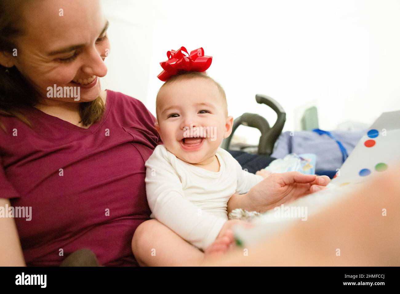Happy Baby si siede nel Lap della mamma sorridendo con l'arco rosso sulla testa Foto Stock