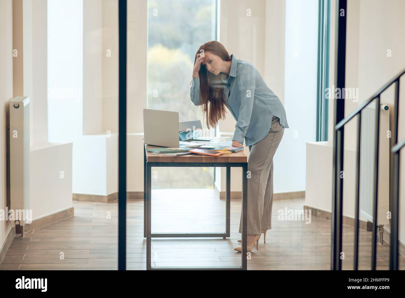 Donna in piedi appoggiata sopra la scrivania in ufficio Foto Stock