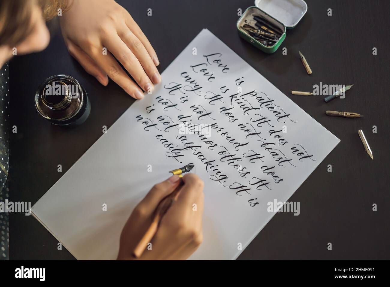 Calligrapher mani scrive una frase sul libro bianco. La Bibbia la frase su amore inscrivendo ornamentali in lettere decorate. La calligrafia, graphic design Foto Stock