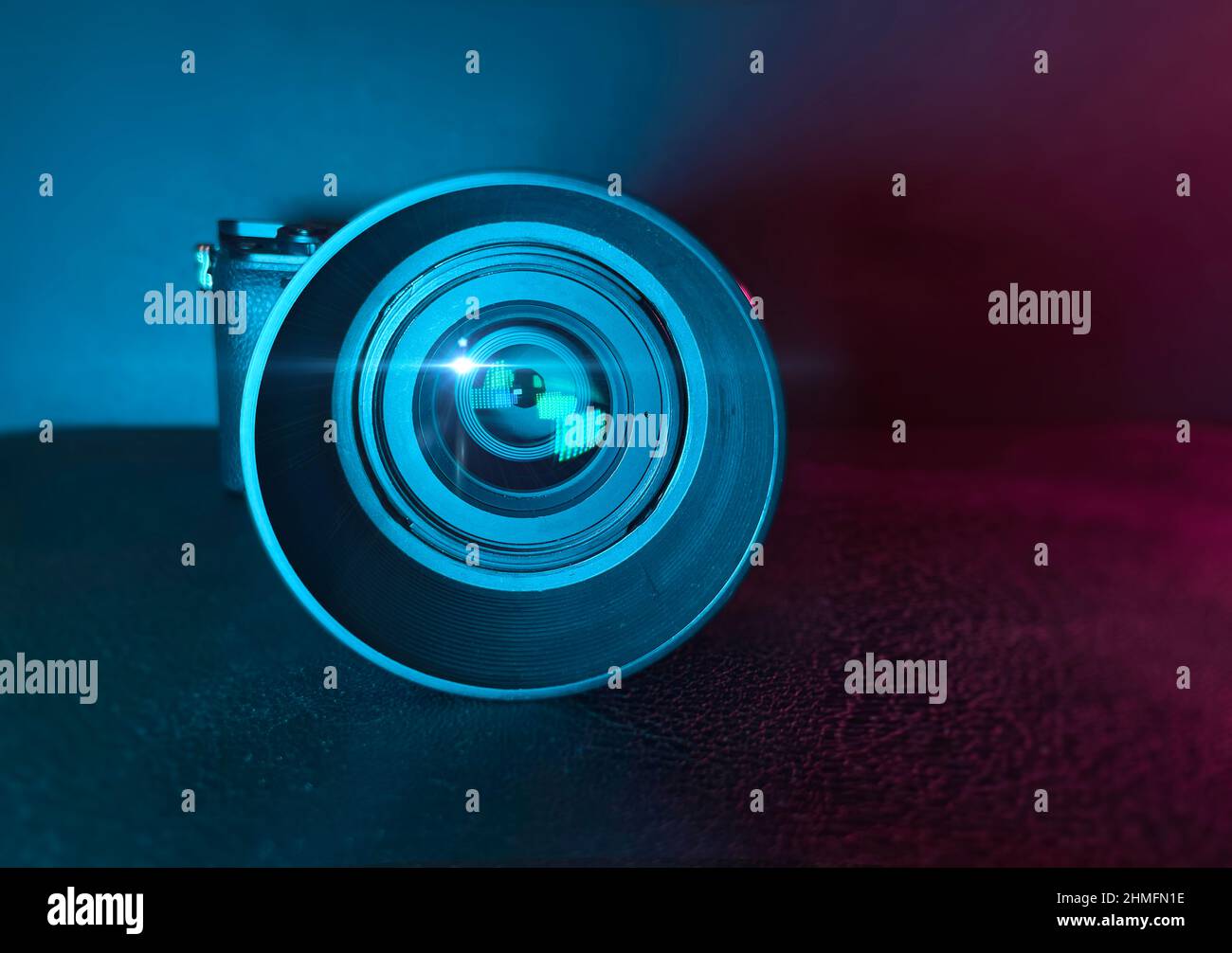 Fotocamera digitale professionale e obiettivo su superficie nera con illuminazione a colori Foto Stock