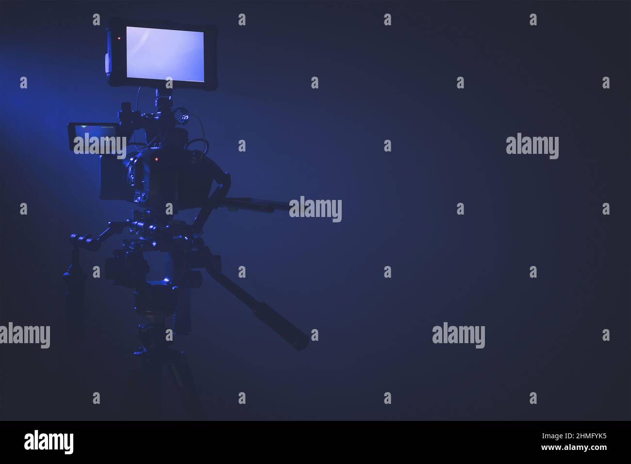 Moderna fotocamera digitale con display esterno che si trova su un cavalletto all'interno dello studio illuminato in blu scuro. Spazio copia lato destro Foto Stock