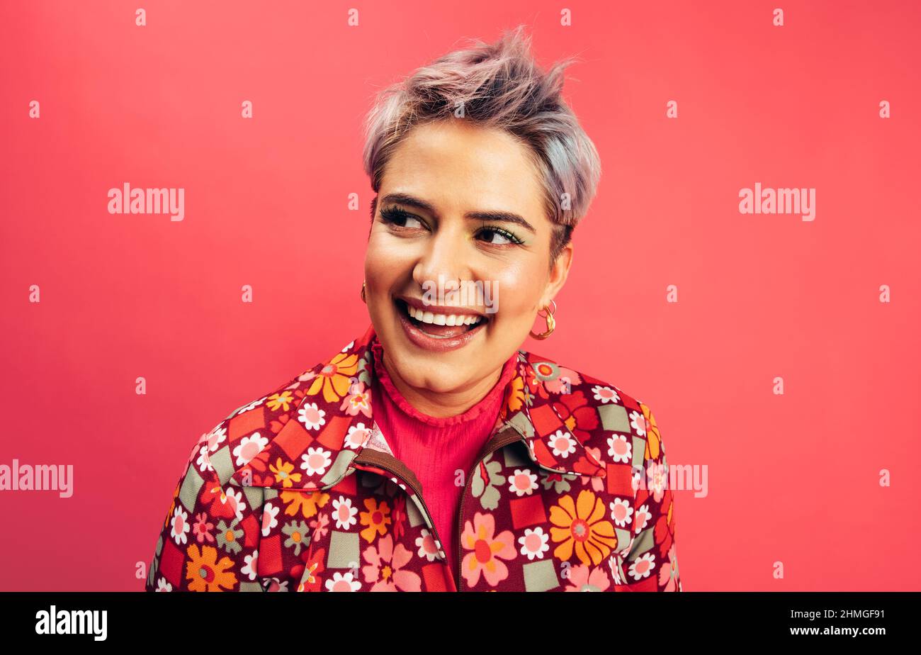 Spensierate la giovane donna che guarda via con un sorriso sul suo volto. Giovane donna felice in piedi da sola su sfondo rosso. Giovane donna alla moda con la ragazza Foto Stock