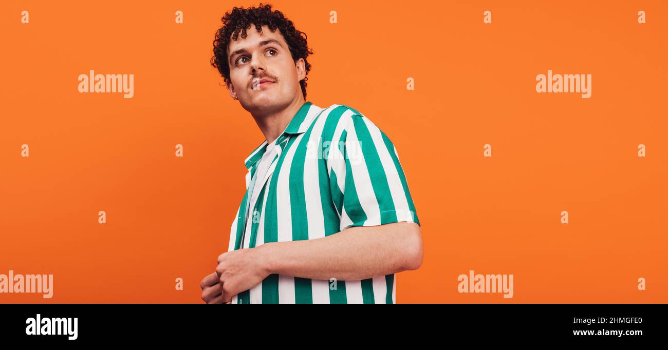 Giovane queer man che guarda via con attenzione in uno studio. Sicuro germello di giovane generazione z in piedi da solo su uno sfondo arancione. Foto Stock