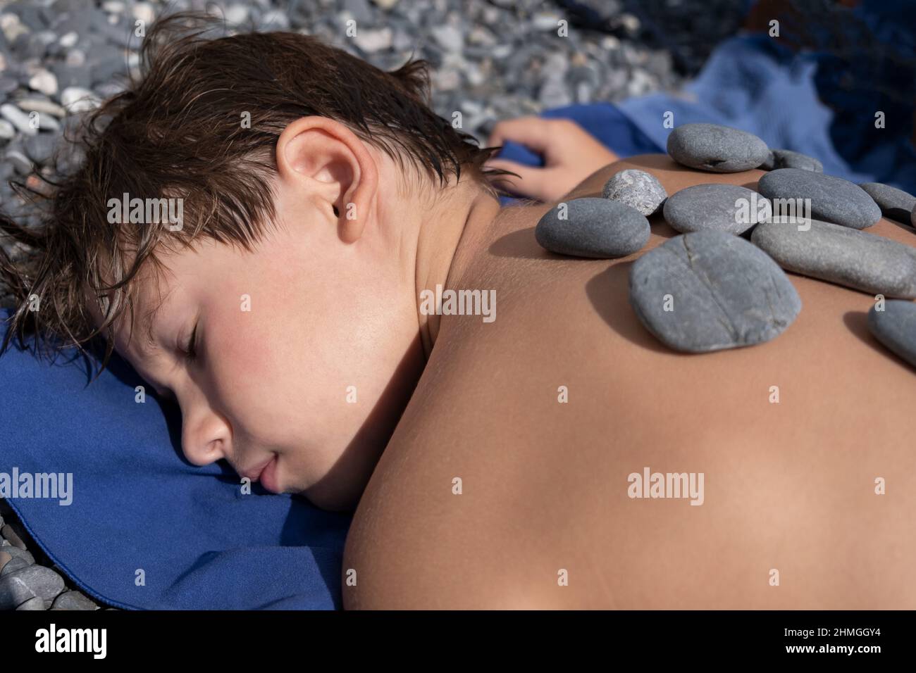 Il ragazzo si trova su una spiaggia di ciottoli. Terapia della pietra. Relax, bambini Mantal Salute. Rilassatevi. Dom Foto Stock