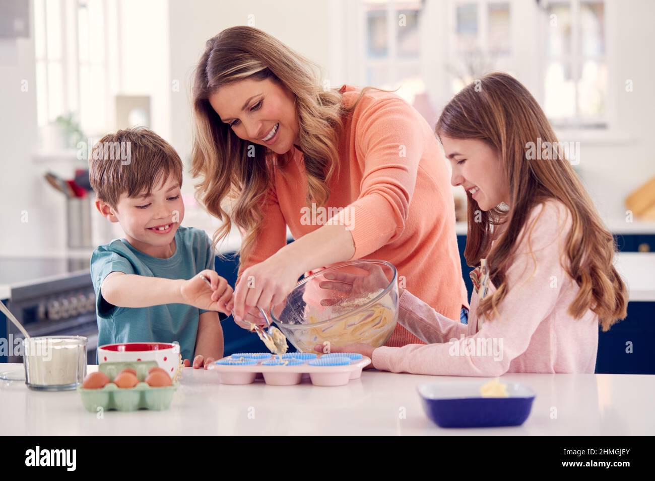 Madre con due bambini in cucina a casa che hanno torte divertenti da forno insieme Foto Stock