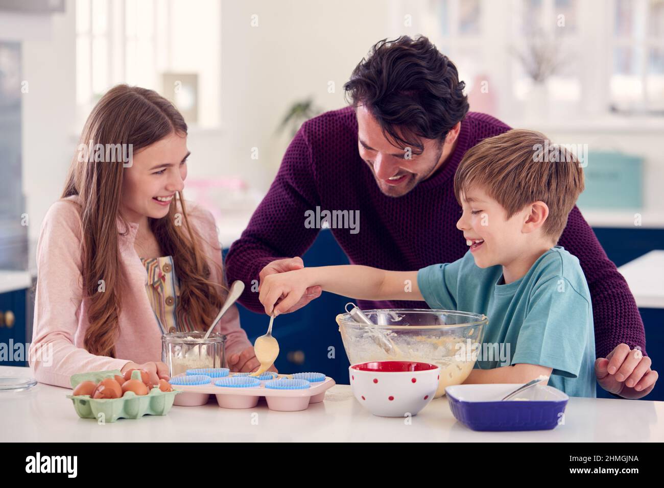 Padre con due bambini in cucina a casa che hanno dolci da forno divertenti insieme Foto Stock