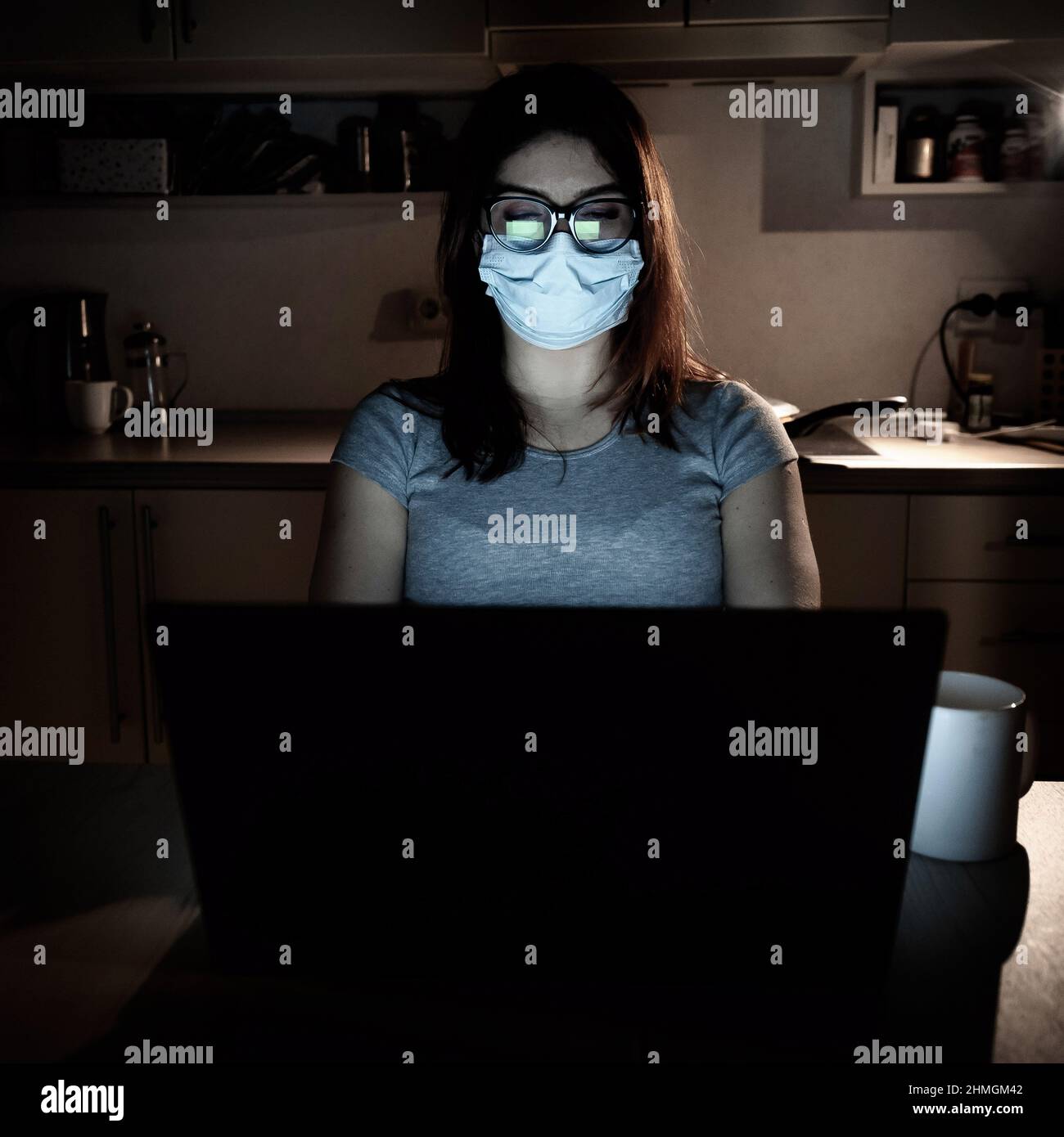 Una ragazza in una maschera e guanti impara durante la quarantena. Una donna che lavora fuori orario da casa su un notebook. Un freelance è seduto in cucina nel Foto Stock