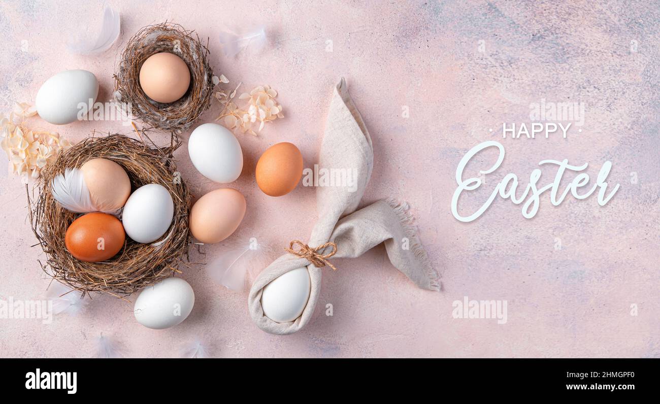 Sfondo pasquale con uova in un nido e un coniglietto pasquale da un tovagliolo su un morbido sfondo rosa. Il concetto di Buona Pasqua. Vista dall'alto. Foto Stock