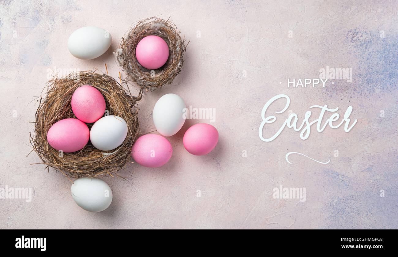 Buona Pasqua, uova colorate rosa e bianche in nidi su un delicato sfondo rosa. Pasqua, sfondo primaverile. Vista dall'alto. Foto Stock