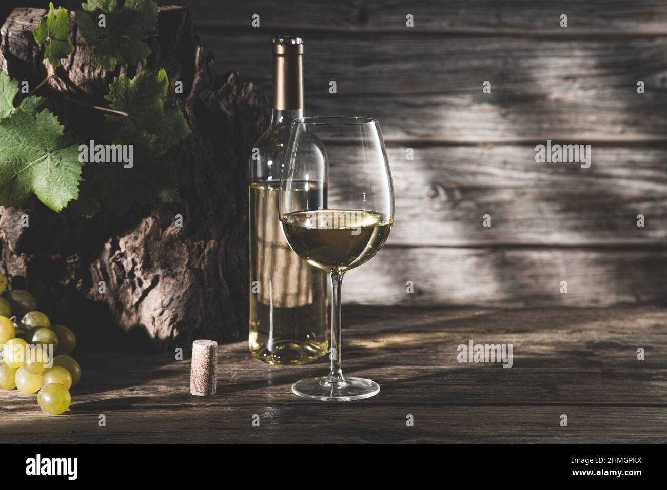 Elegante bicchiere di vino e bottiglia di vino bianco con uva e ombre su sfondo di legno scuro con copyspace. Foto Stock