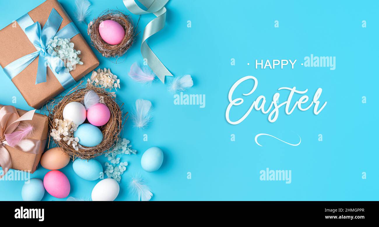 Festivo, sfondo pasquale con regali, uova in un nido, fiori e piume su sfondo blu. Il concetto di Buona Pasqua. Foto Stock