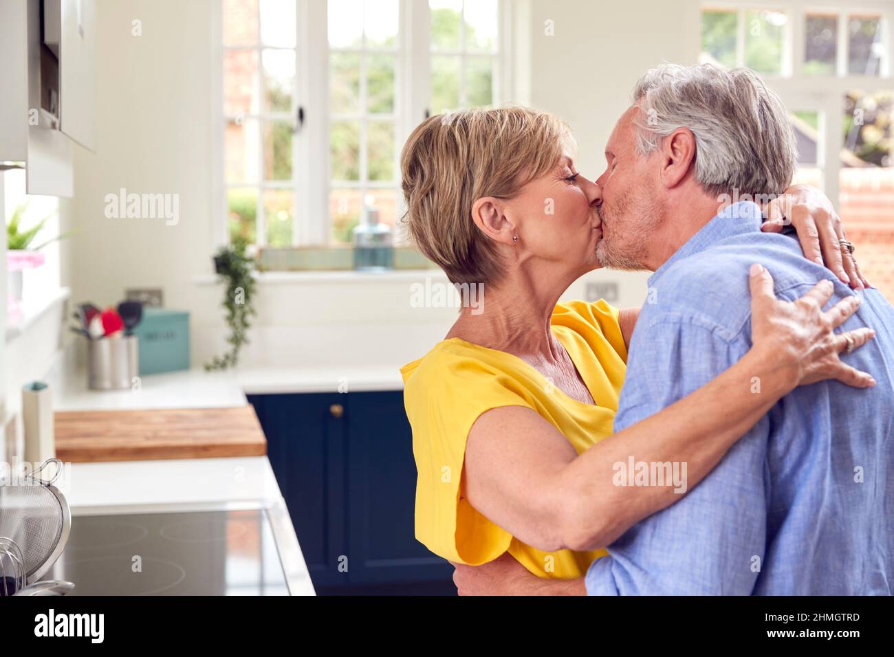 Amorevole coppia pensionato abbraccio e baciare in cucina a casa insieme Foto Stock
