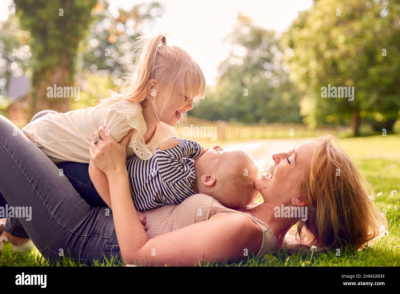 Madre e bambini che hanno divertimento all'aperto con i bambini che si trovano sopra di lei su erba Foto Stock