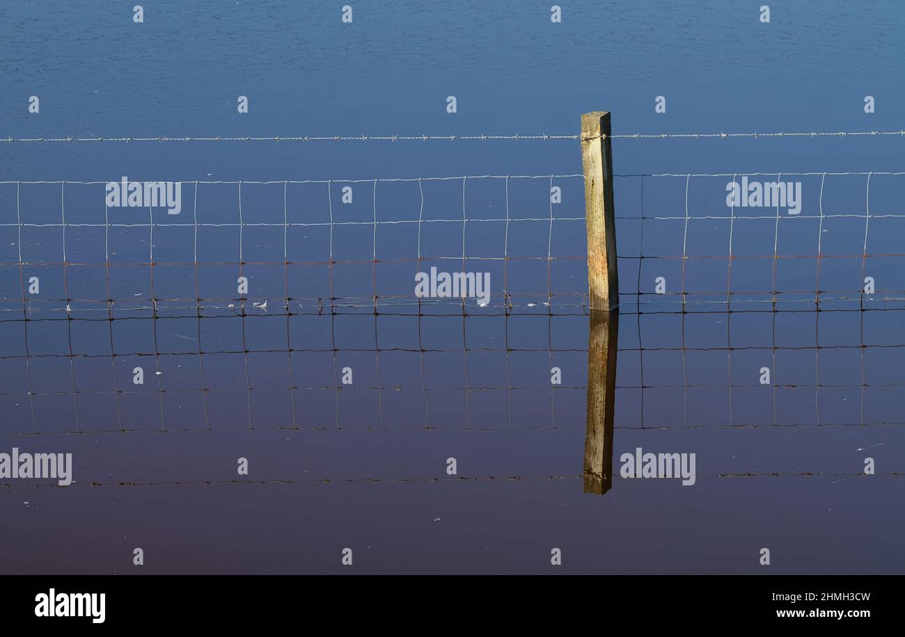 Immagine minimalista di una riflessione di un singolo palo di fence e rete metallica in Blue Sea Water Lagoon, Keyhaven UK Foto Stock
