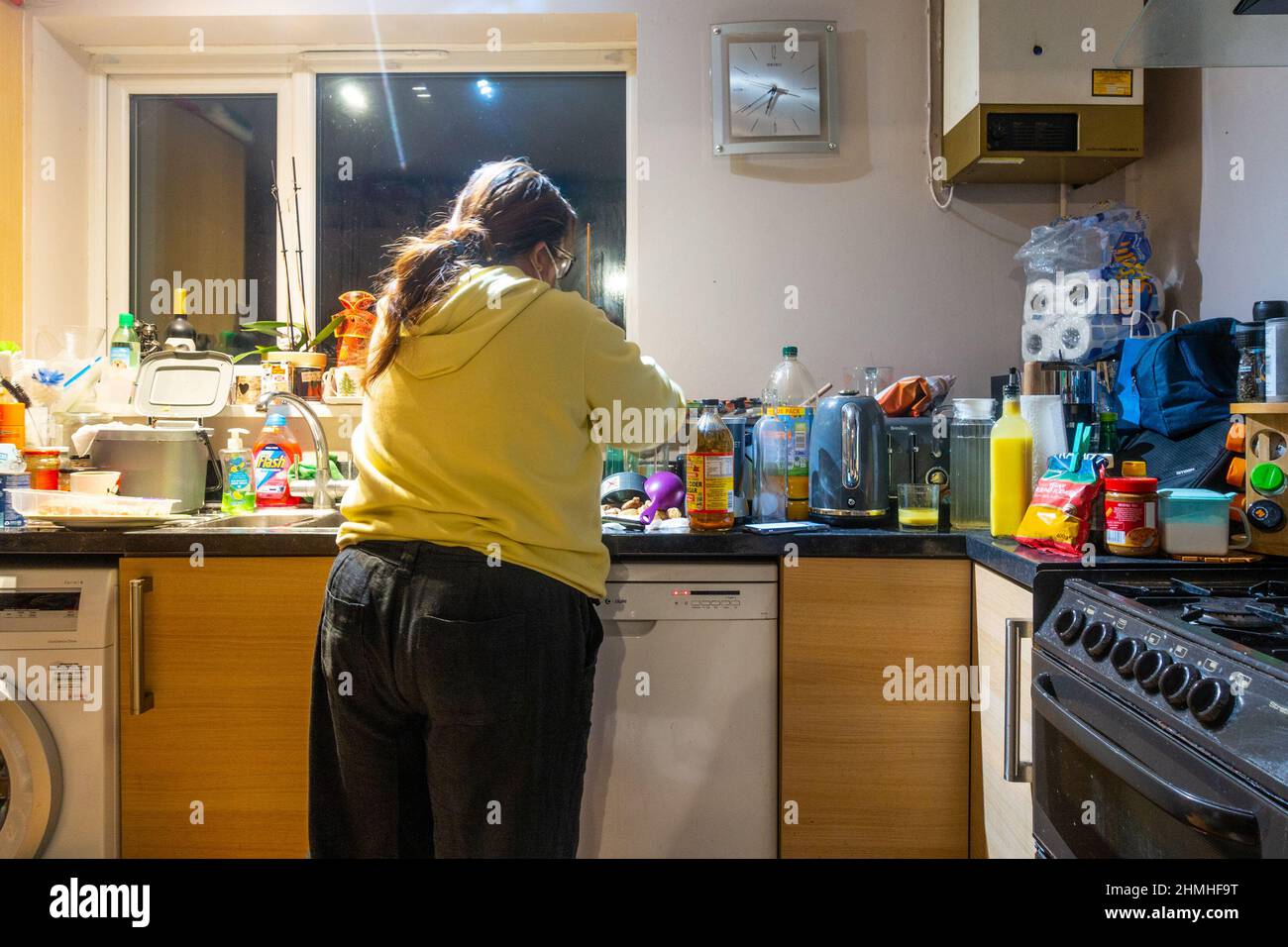 Una donna che prepara il cibo in una cucina occupata con un sacco di ammasso sui piani di lavoro/ Foto Stock