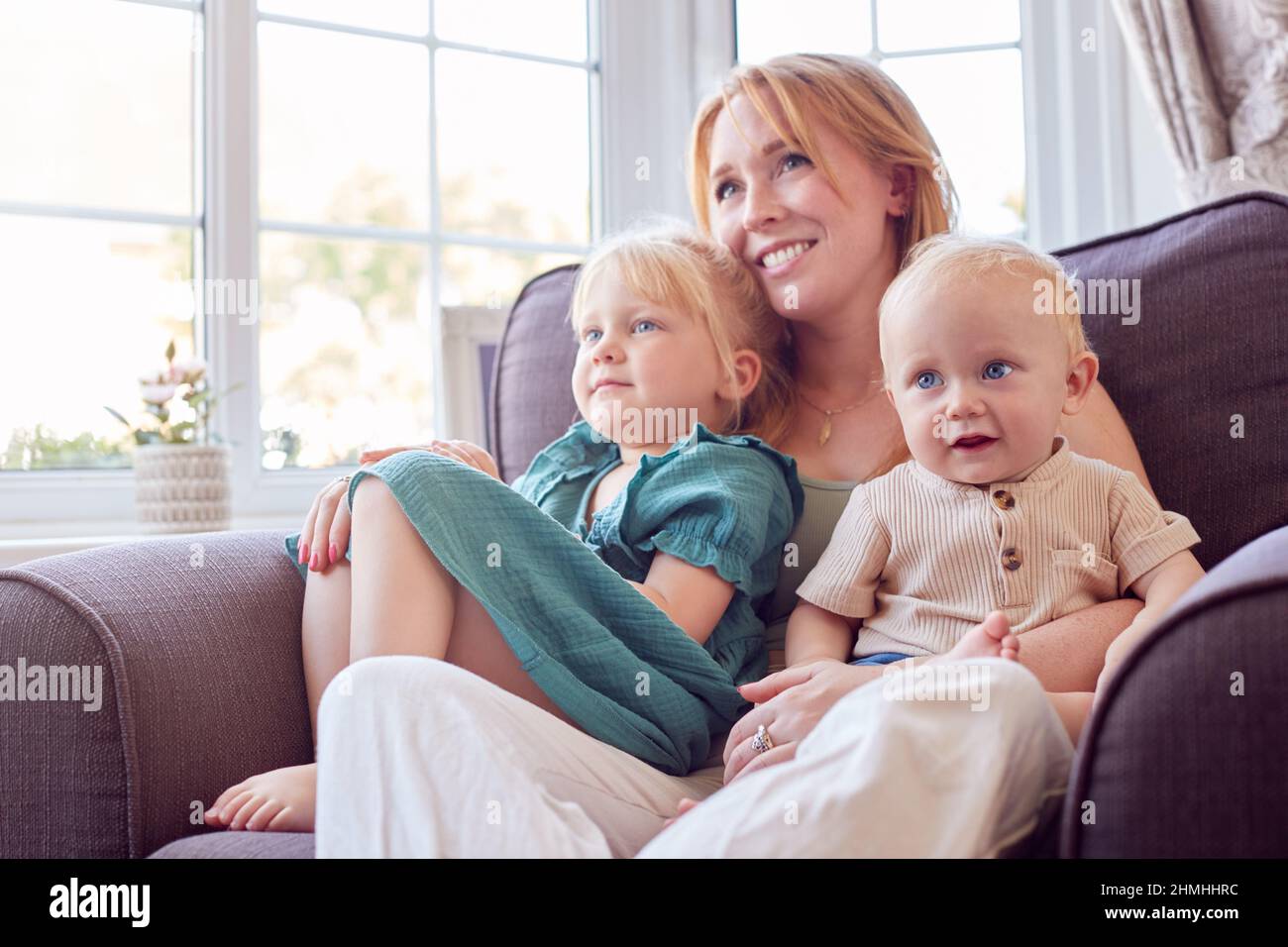 Madre con due bambini seduti sul divano in salotto a casa guardando la TV insieme Foto Stock