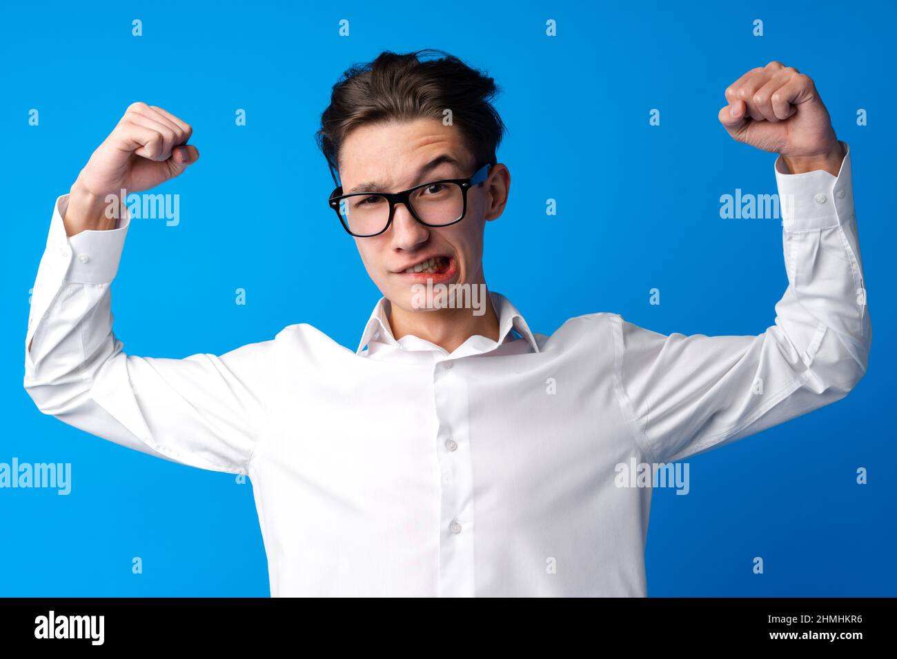 Ragazzo allegro adolescenti in occhiali dimostrando bicipiti su sfondo blu Foto Stock