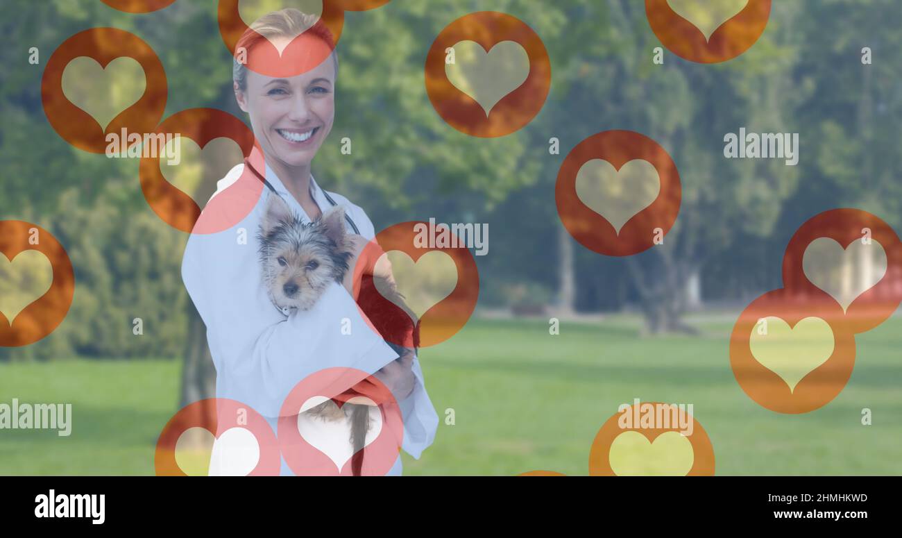 Immagine di icone di cuore che si muovono su sorridente femmina vet tenendo cane Foto Stock