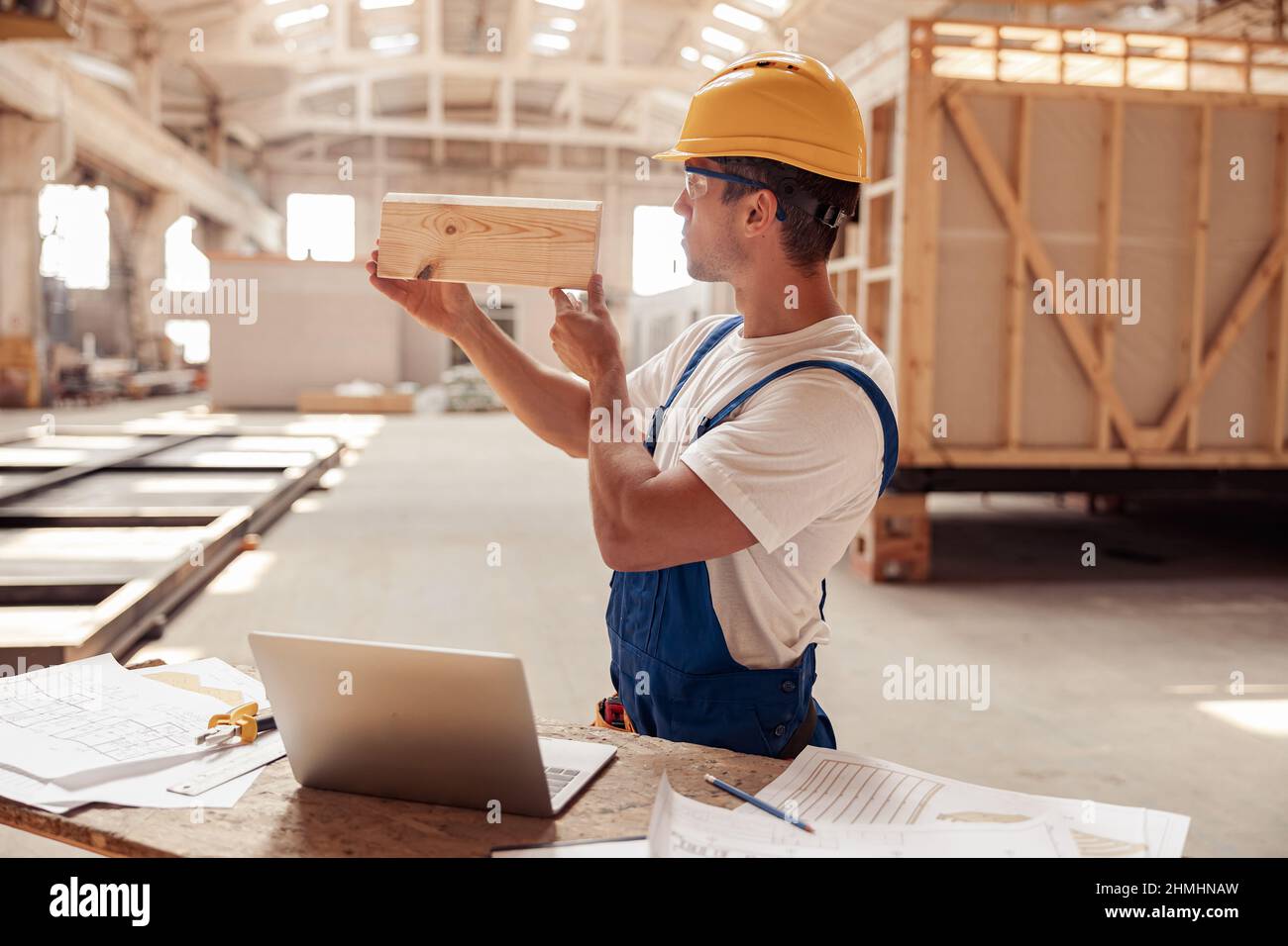 Costruttore maschio che controlla asse di legno in cantiere Foto Stock