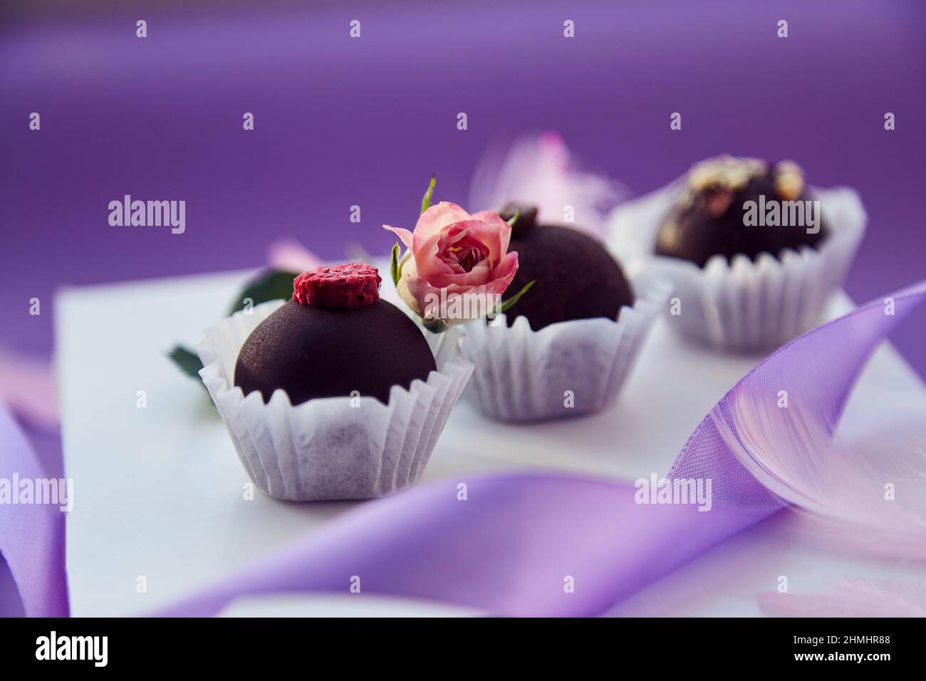 Caramelle al cioccolato festive. Delicate piume rosa e nastro viola. Sfondo con motivo di colore viola. Foto Stock