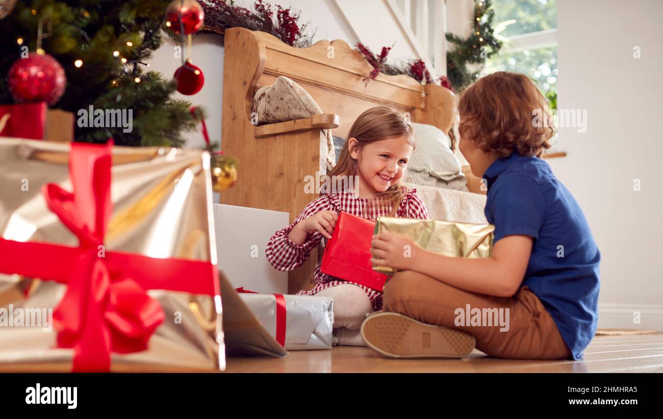 Due bambini eccitati che scuotono e si sentono presenta sotto l'albero di Natale a casa Foto Stock