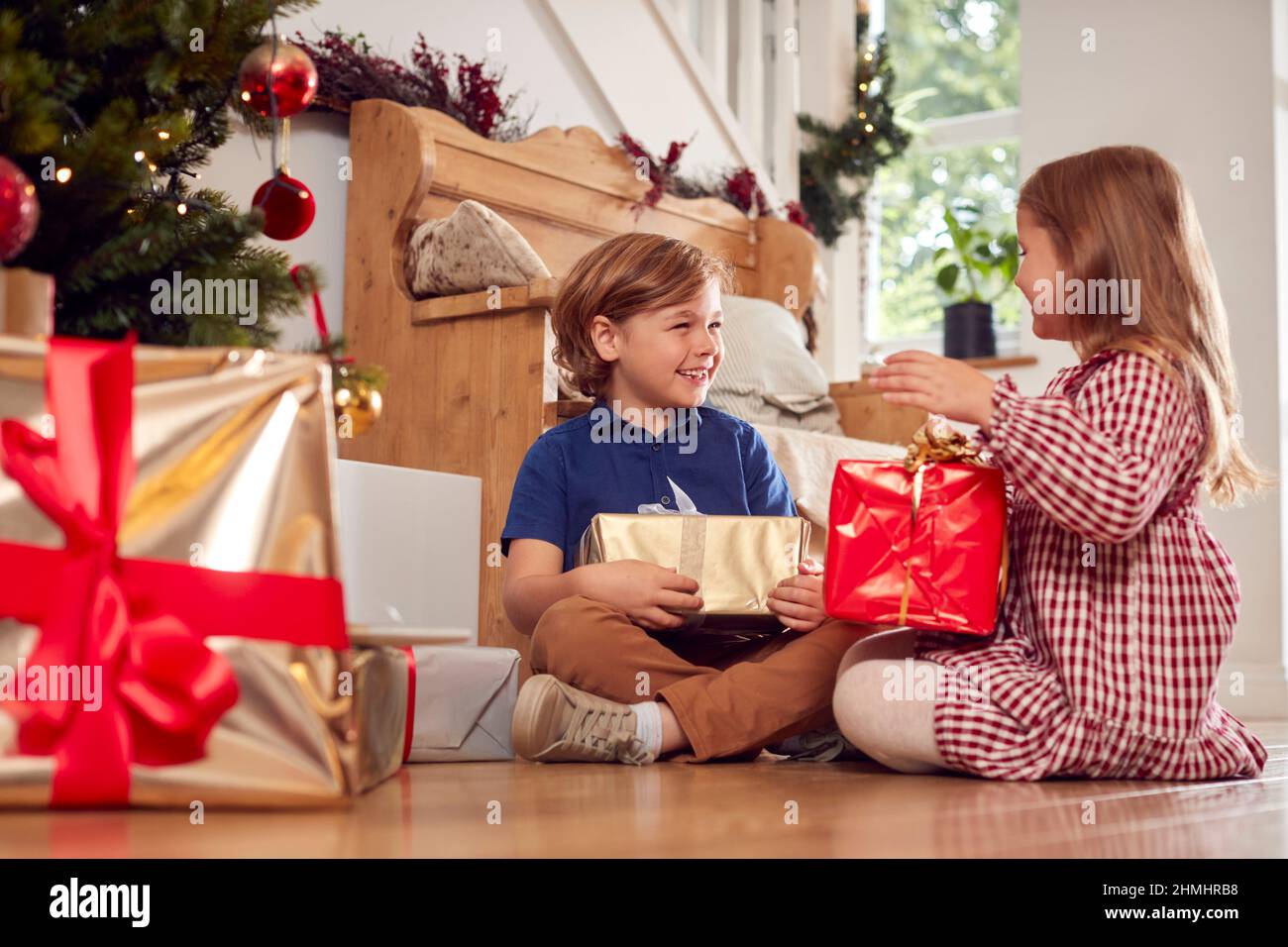 Due bambini eccitati che scuotono e si sentono presenta sotto l'albero di Natale a casa Foto Stock