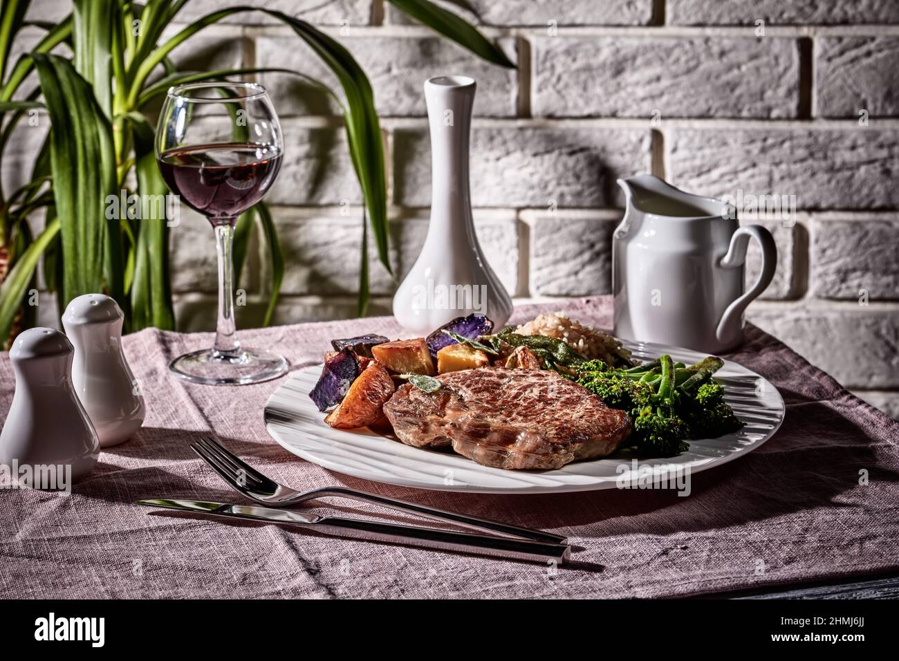 Bistecca di manzo con un bicchiere di vino rosso servito con broccolini, riso e patate arcobaleno al forno, primo piano Foto Stock