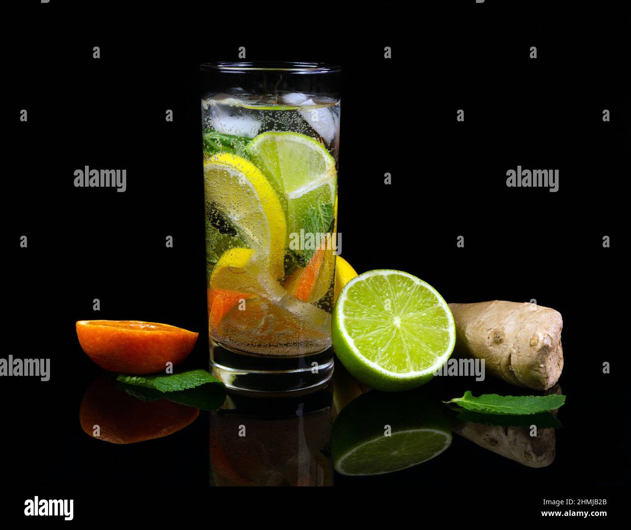 Bicchiere di limonata fresca e pezzi di frutta tagliata al limone su sfondo nero riflettente Foto Stock