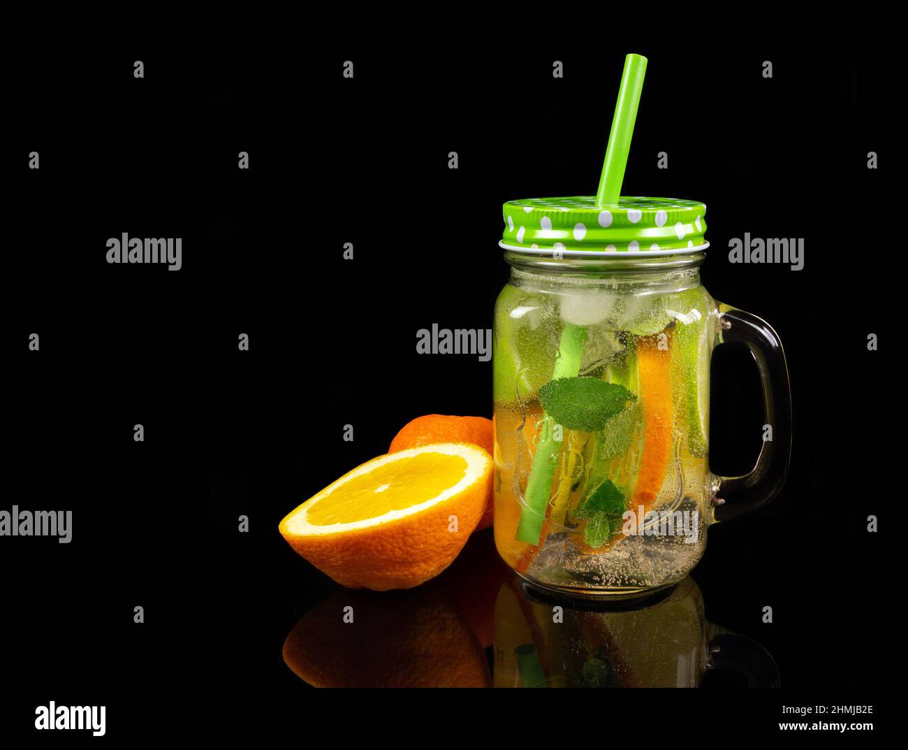 Vasetto di limonata fresca e pezzi di frutta tagliata al limone su sfondo nero riflettente Foto Stock