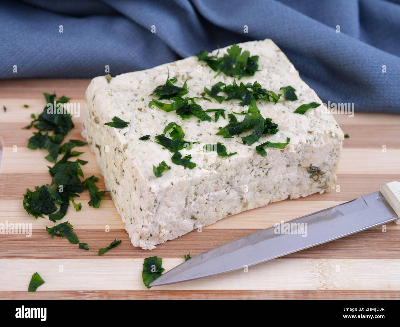 Un blocco di tofu con un po' di prezzemolo adagiato su un tagliere. Primo piano. Foto Stock