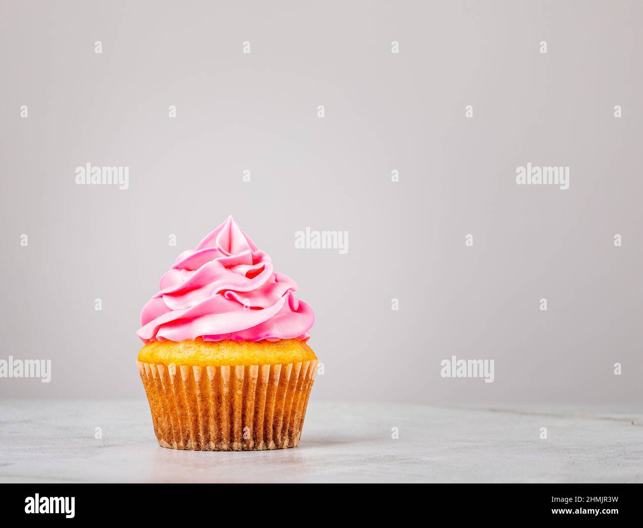 Cupcake alla vaniglia con glassa rosa di crema di burro sul grigio. Foto Stock