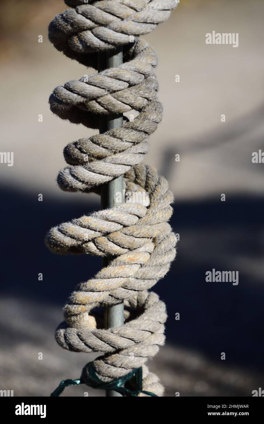 Su uno sfondo di colore scuro, una spessa corda in fibre naturali avvolta intorno ad un'asta metallica in formato ritratto Foto Stock