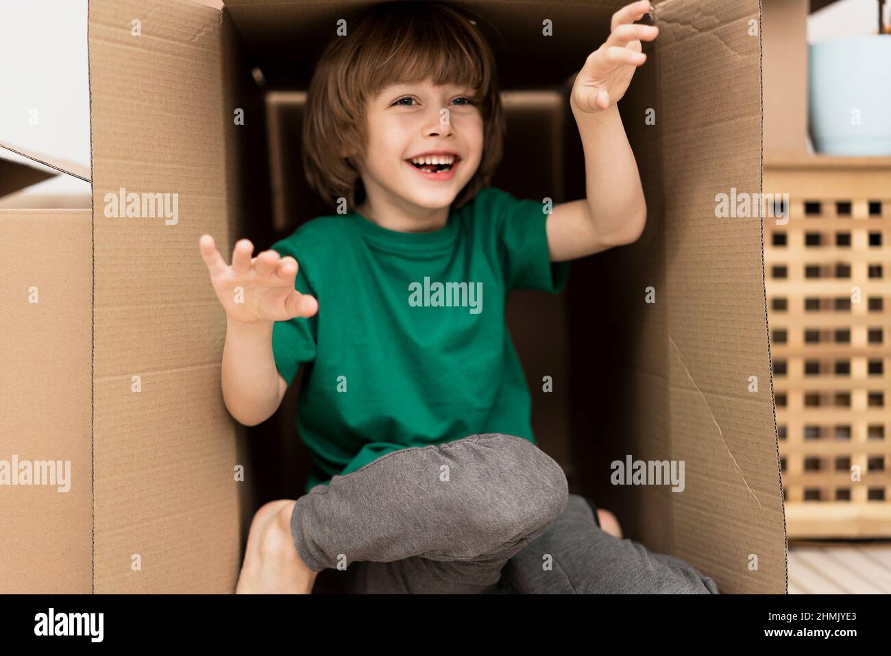 Ragazzo che si nasconde all'interno di un'enorme scatola di cartone. Sta giocando e guardando fuori da una scatola. Il capretto è felice di muoversi in una nuova sede. Foto Stock