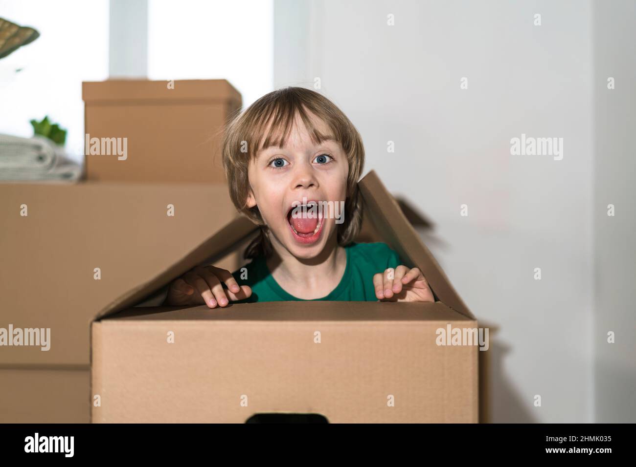 Il ragazzino eccitato che salta all'interno di un'enorme scatola di cartone. Sta giocando e guardando fuori da una scatola. Il capretto è felice di muoversi in una nuova sede. Foto Stock
