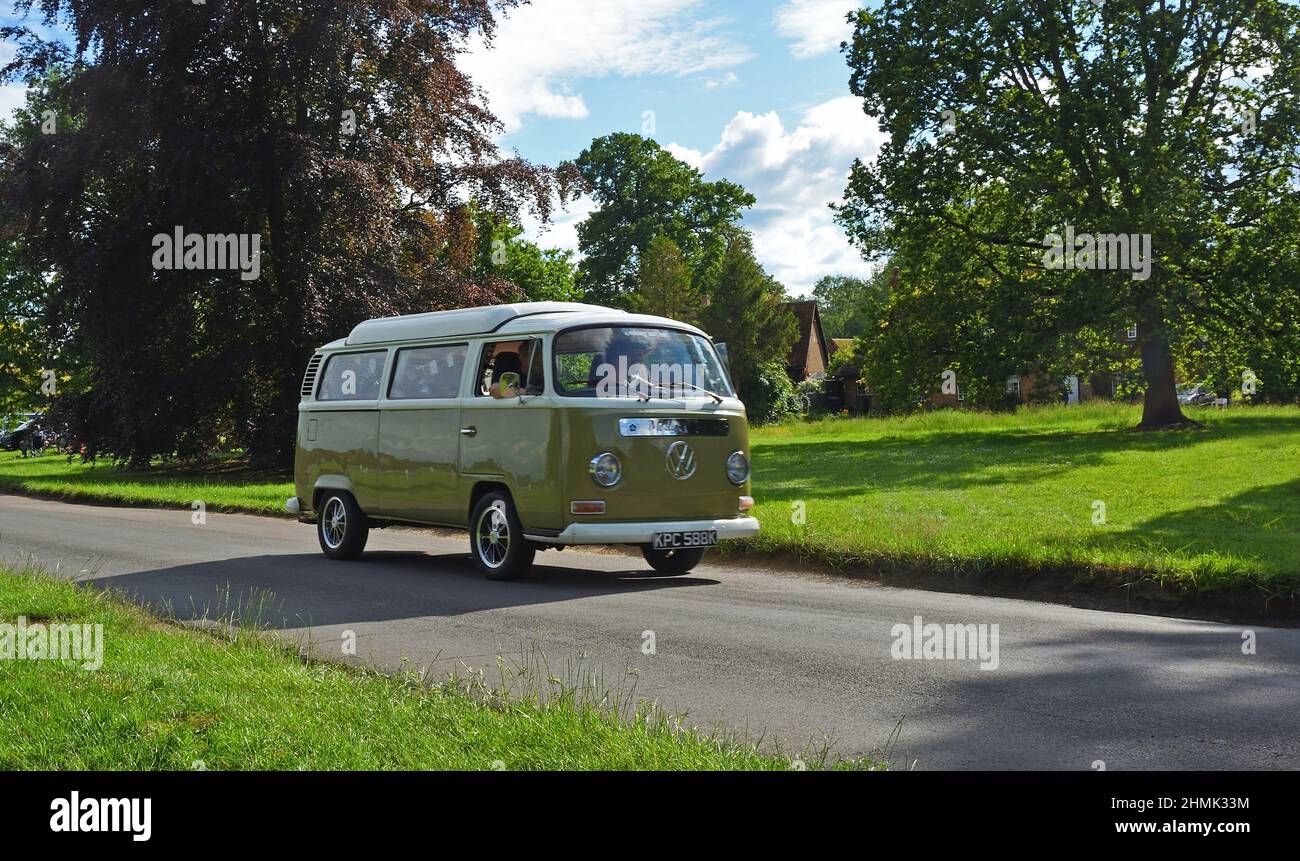 Classic Volkswagen Camper Van guidando attraverso cottage villaggio e alberi sullo sfondo. Foto Stock