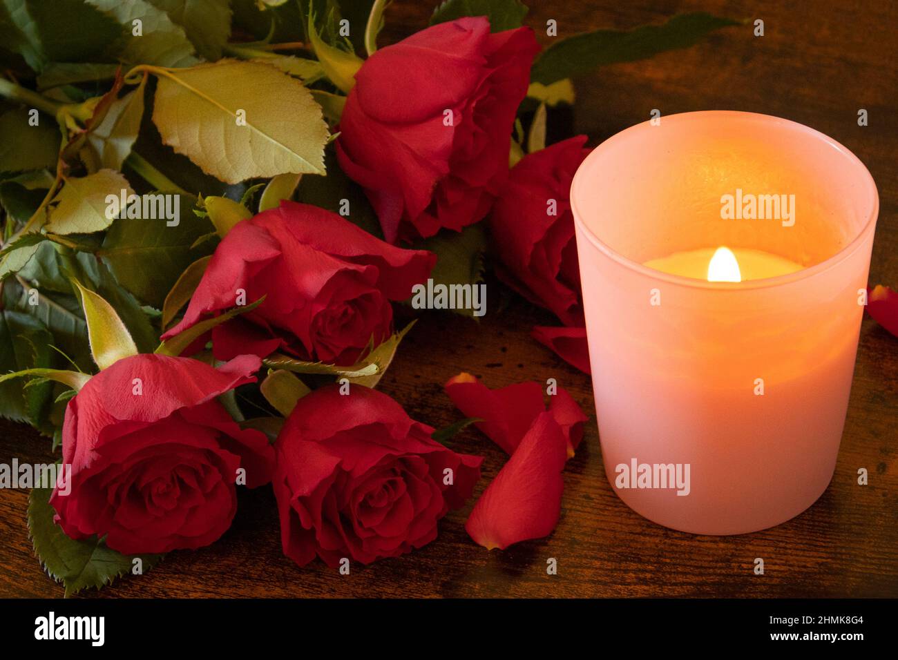 bouquet di rosa rossa con petali e una candela su sfondo di legno Foto  stock - Alamy