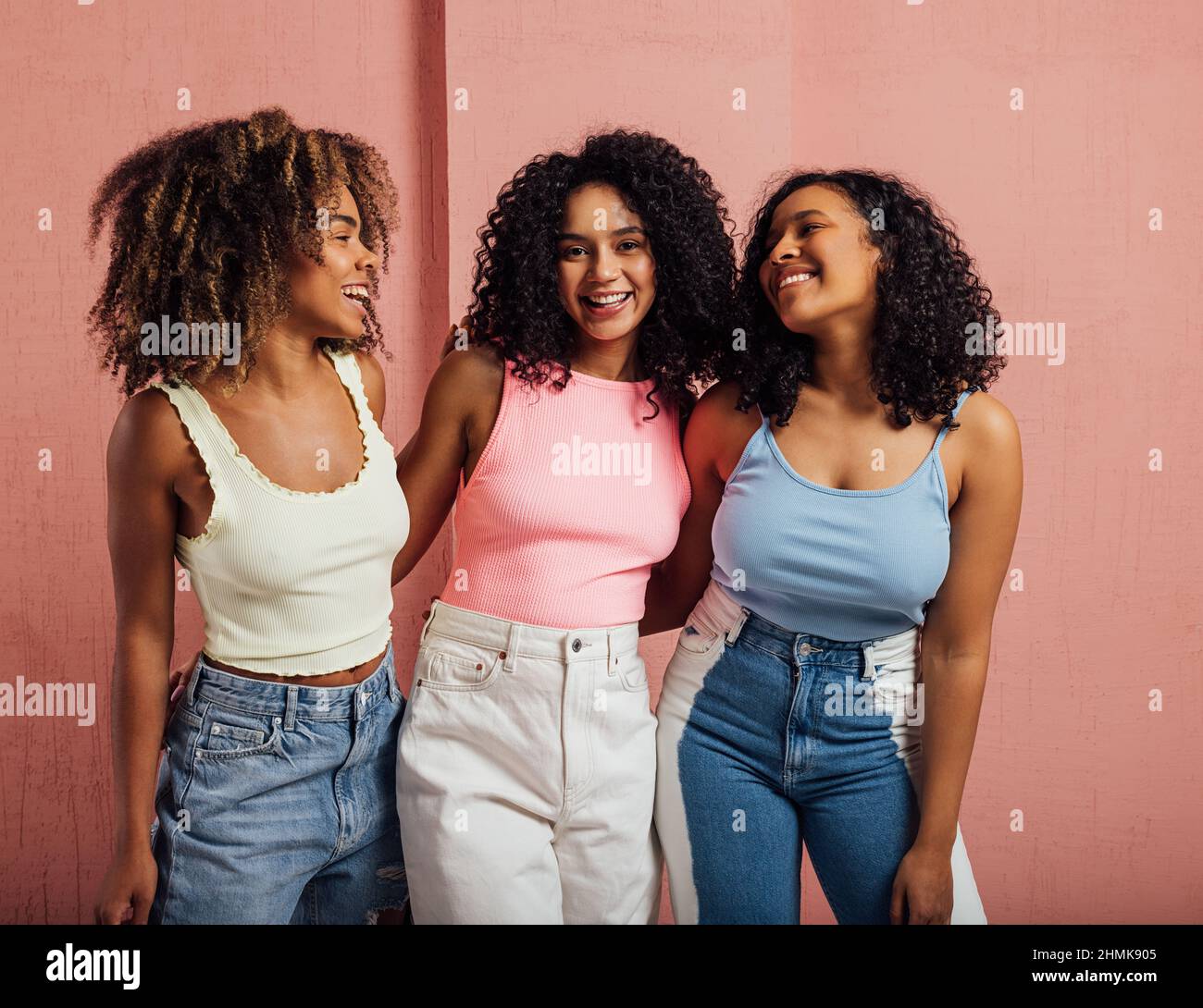 Tre donne allegre con capelli ricci che si divertono insieme in piedi ad una parete rosa Foto Stock