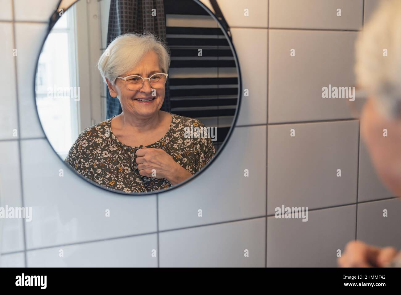 vecchia signora caucasica dai capelli grigi che guarda se stessa nello specchio e sorride . Foto di alta qualità Foto Stock