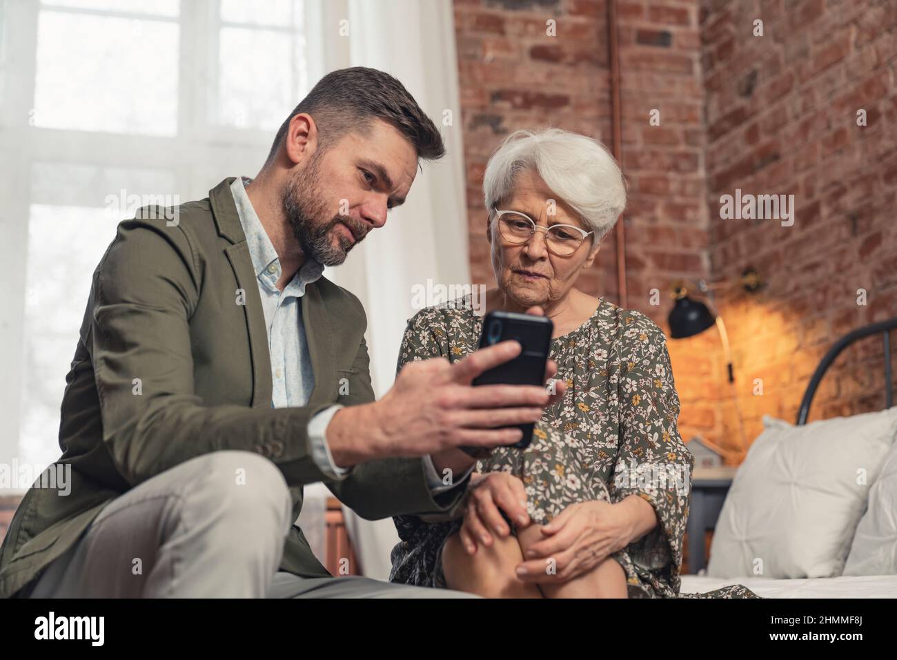 figlio caucasico di mezza età che impara la madre pensionato come usare uno smartphone . Foto di alta qualità Foto Stock