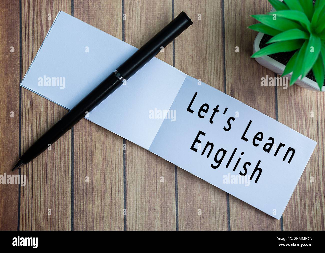 Consente di imparare il testo inglese su blocco note con pianta in vaso su una scrivania di legno Foto Stock