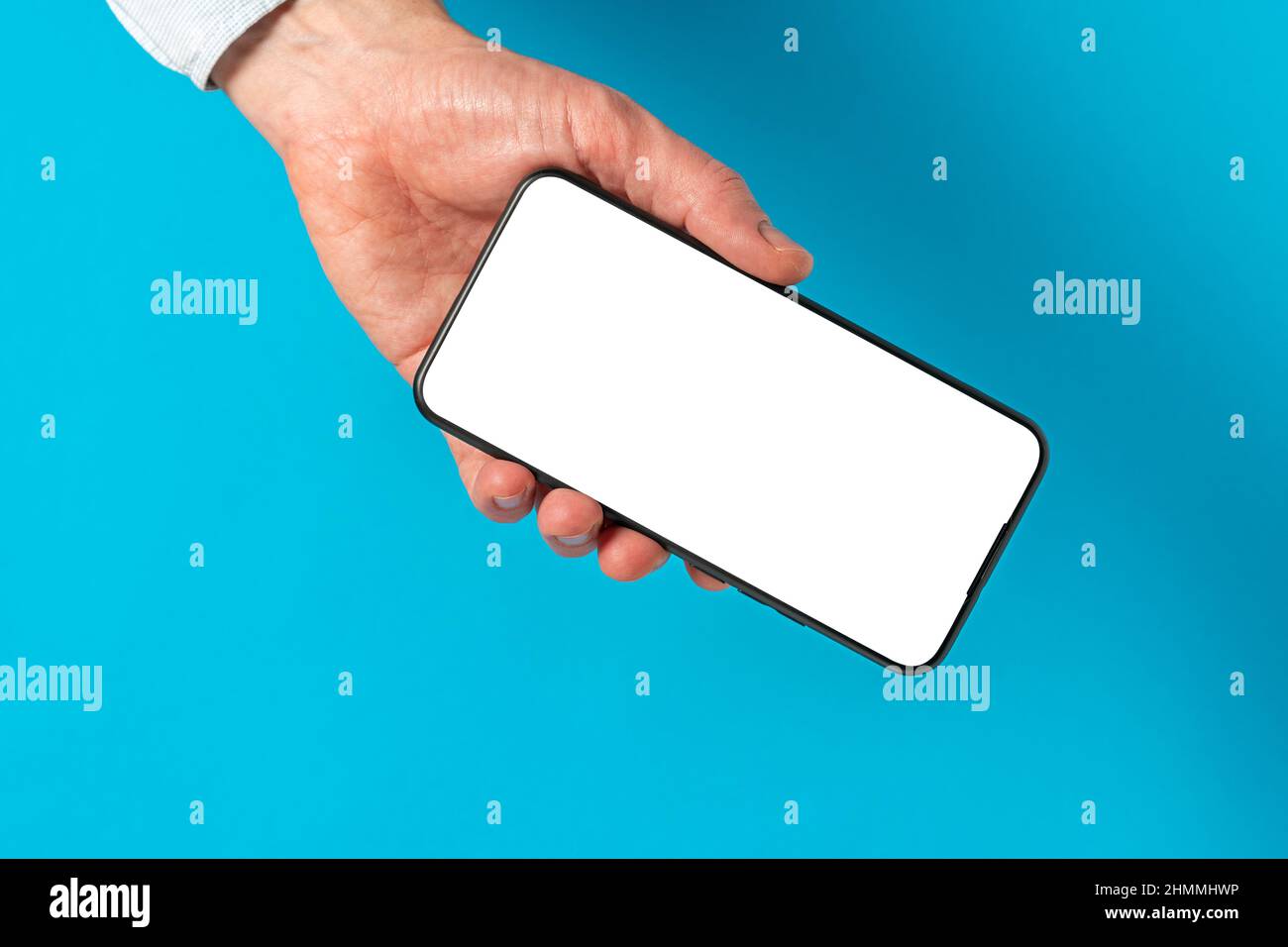 Mano dell'uomo che tiene lo smartphone nero del telefono delle cellule con schermo bianco vuoto. Spazio di copia. Foto Stock