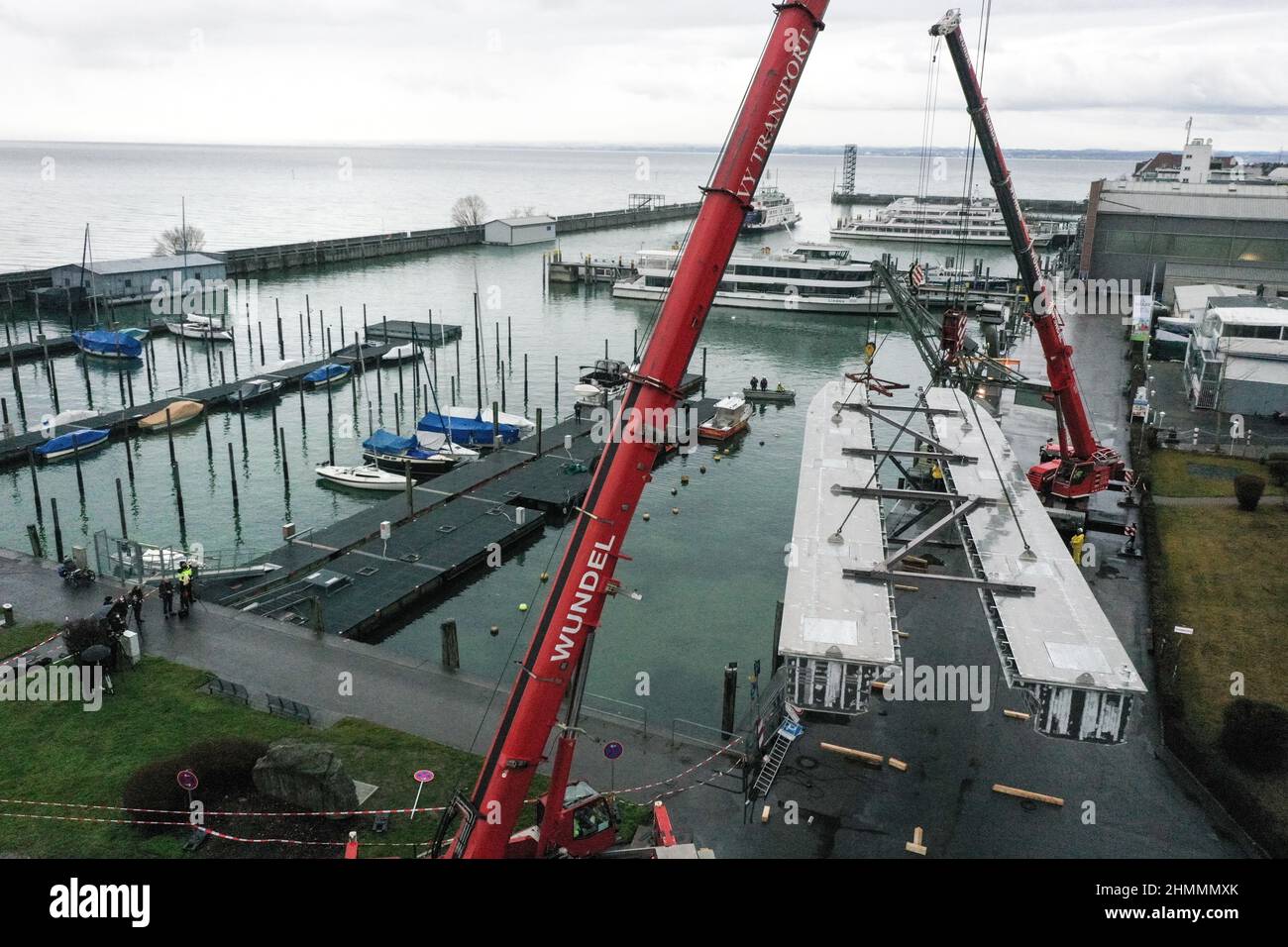 Friedrichshafen, Germania. 11th Feb 2022. Due gru sollevano i due scafi per il futuro catamarano elettronico dalla terraferma nel bacino del porto. Gli scafi pesano circa 20 tonnellate e sono stati costruiti a Stralsund. La mattina, gli scafi arrivarono a Friedrichshafen dal cantiere su un trasportatore pesante. Credit: Felix Kästle/dpa/Alamy Live News Foto Stock