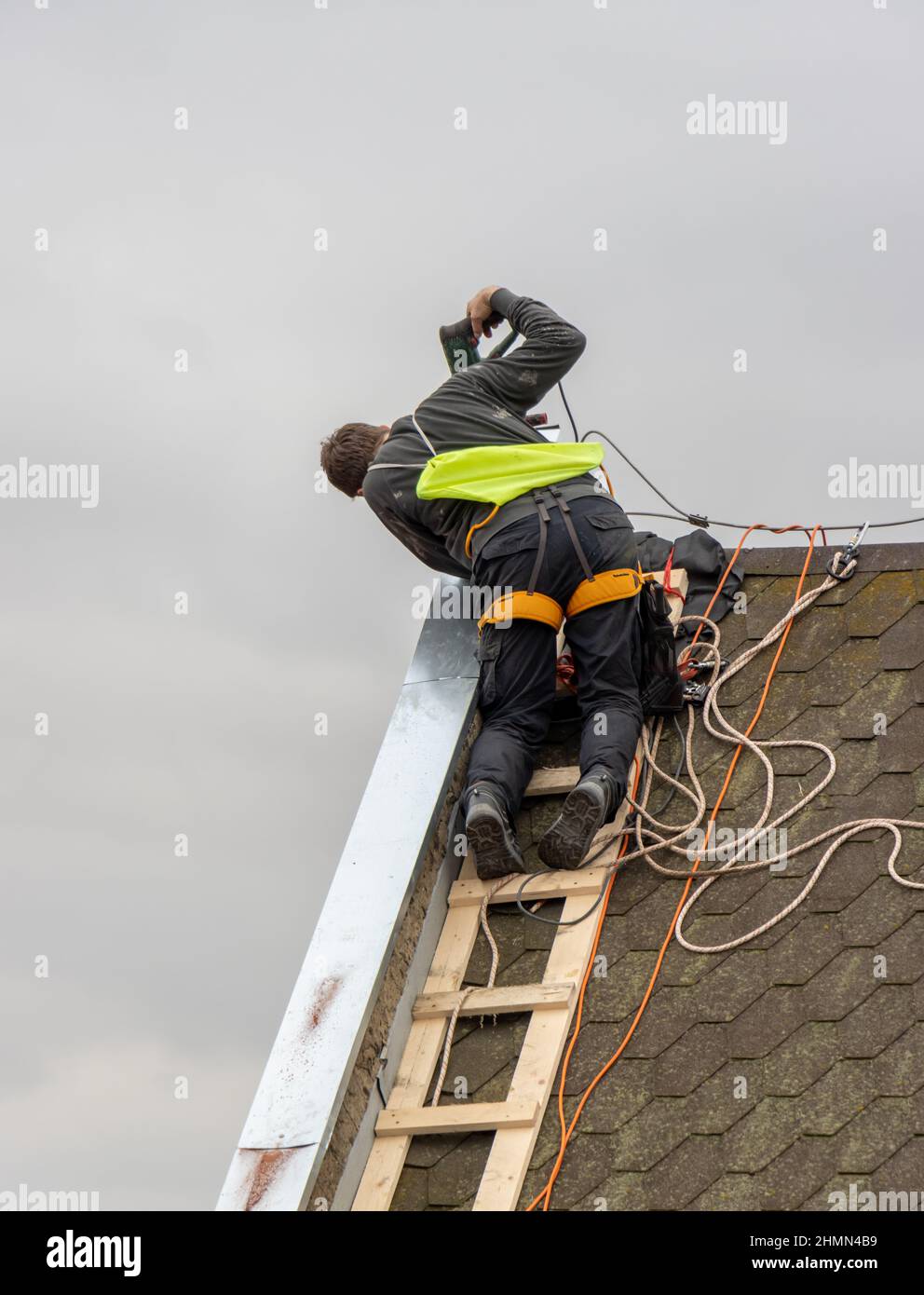 Un uomo lavora sulla riparazione del tetto, installa la lamiera sulla parte superiore della parete del timpano Foto Stock