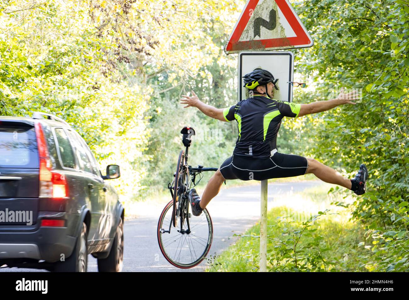Un ciclista che cade urta in un cartello stradale accanto alla strada con traffico Foto Stock