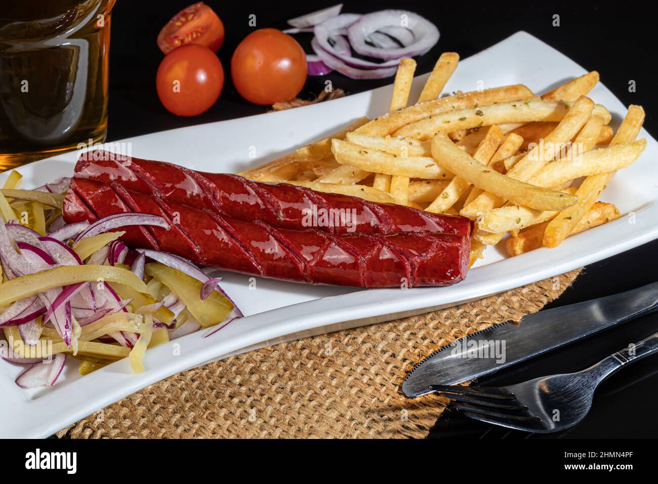 Salsicce affumicate con patatine fritte e sottaceti. Spuntino per la birra. Sfondo scuro. Spazio di copia. Foto Stock