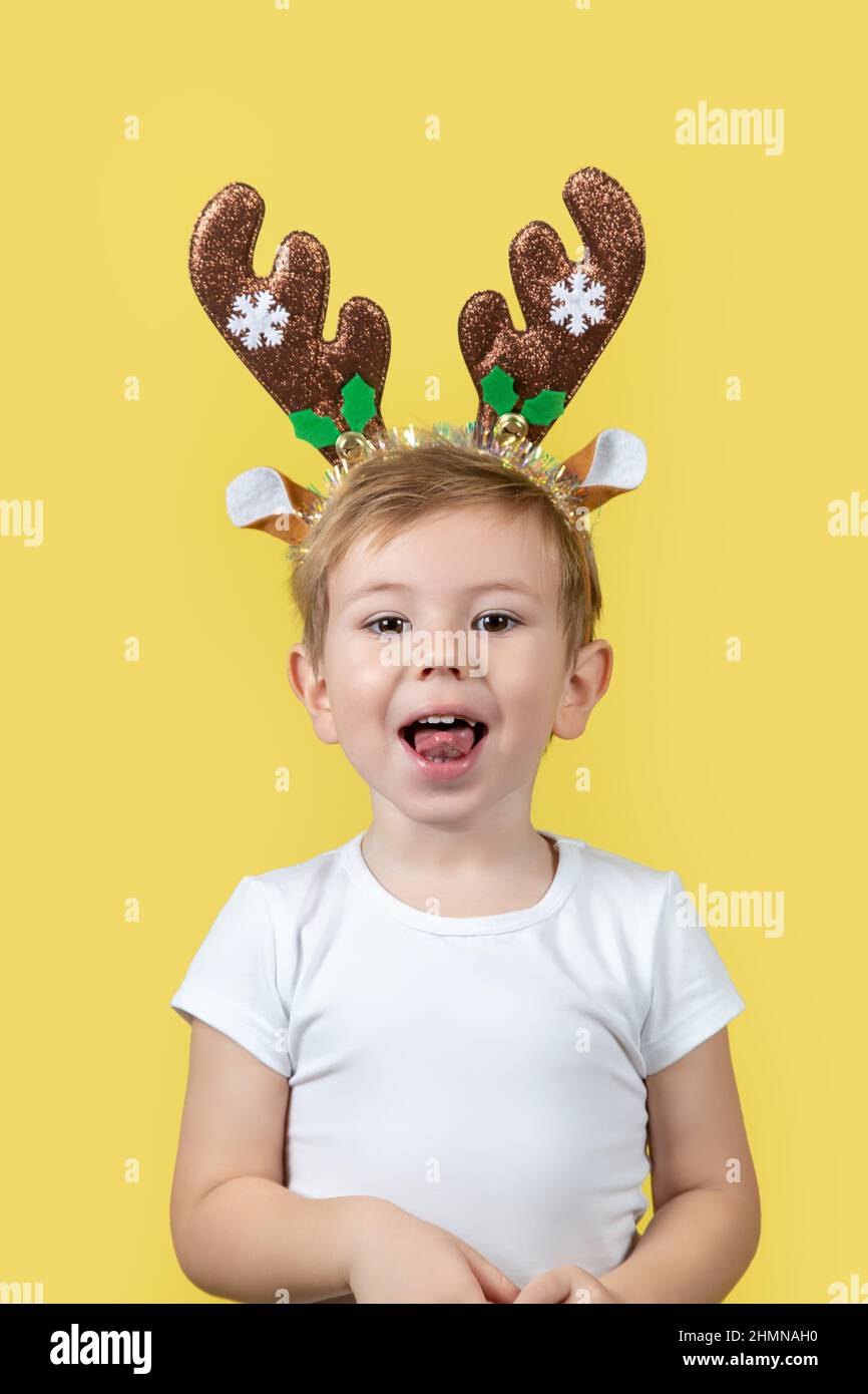 Carino ragazzo caucasico in costume da renna di natale con sveglie nelle sue mani facendo volti divertenti. Un luogo per il testo. Studio girato su un giallo Foto Stock