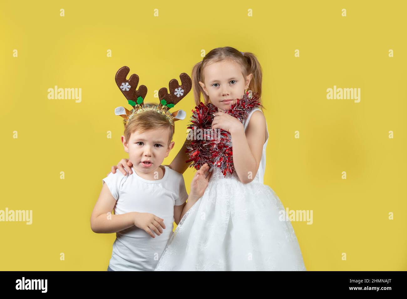 Ritratto di bambini carini in costume da renna di natale e bel vestito guardando la macchina fotografica su uno sfondo giallo, preparando per il nuovo Yea Foto Stock